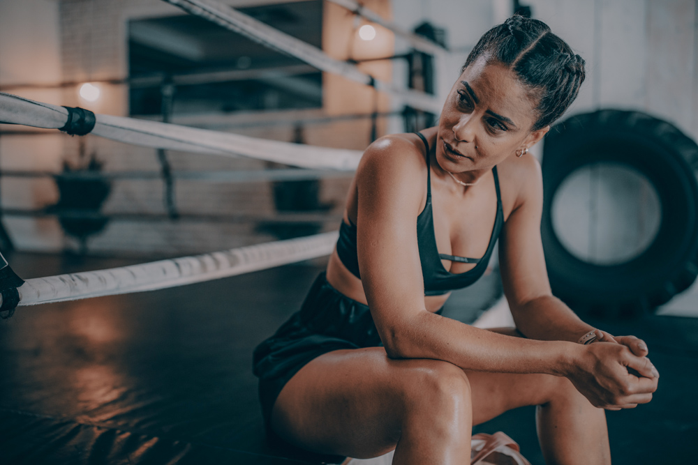 WOMAN SITTING ON THE SIDE OF A BOXING RING WITH BLACK SPORTS BRA