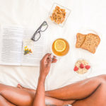 Woman sitting in bed reading with food. Morning routine.